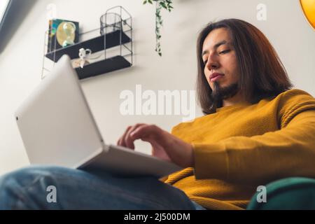 Un homme caucasien attrayant est assis sur le canapé, travaillant sur un ordinateur portable, travaillant à la maison, à distance concept de travail copie espace . Photo de haute qualité Banque D'Images