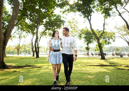 Couple multiethnique marchant tout en embrassant se regardant dans un parc Banque D'Images