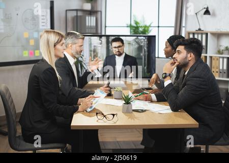 Entreprise, concept de travail d'équipe. Groupe de partenaires professionnels internationaux ciblés, discutant des détails du projet commun dans une salle de réunion moderne pendant la vidéoconférence. Télécréation. Banque D'Images