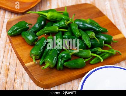 Poivrons padron verts frais sur planche à découper en bois Banque D'Images