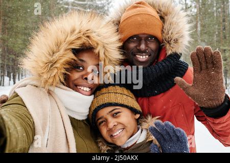 La famille afro-américaine de trois enfants en hiver vous accueille tout en regardant l'appareil photo dans le parc ou la forêt lors d'une journée hivernale glaciale à votre guise Banque D'Images