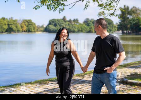 Couple multiethnique formé par une femme andine et un homme caucasien marchant au bord d'un lac. Expressions et visages heureux des amoureux Banque D'Images