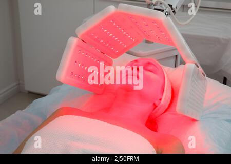 Une femme âgée subit une procédure de rajeunissement du visage. Femme visage LT traitement de lumière rouge à la clinique de beauté. Cosmétologie. Banque D'Images