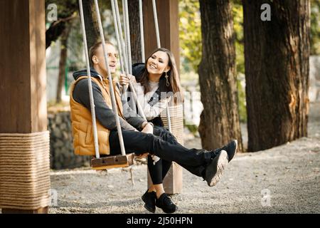 Vue latérale d'un jeune couple aimant assis sur balançoire dans le parc à l'extérieur. Photo de haute qualité Banque D'Images