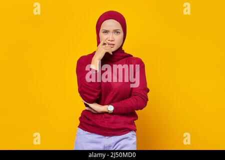 Portrait de la jeune femme asiatique stressée et nerveuse avec les mains dans la bouche mordant des ongles isolés sur fond jaune Banque D'Images