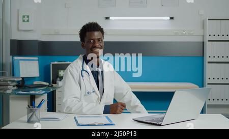 Un médecin portant un uniforme médical assis au bureau avec un ordinateur portable moderne, des dossiers de documents et du matériel de santé au bureau de la clinique médicale.Un appareil photo professionnel digne d'une médaille Banque D'Images