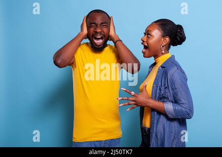 Petite amie criant à l'homme couvrant ses oreilles pour arrêter de se querler, exprimant la frustration. Couple malheureux se battant et criant en studio, ayant des problèmes de relation. Bouleverser les personnes en conflit. Banque D'Images