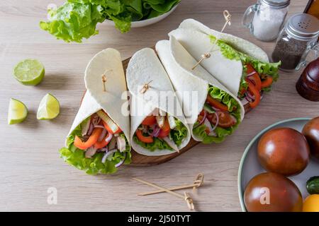 des légumes frais hachés et des filets de poulet emballés dans des tortillas maison sont sur un panneau de bois. les ingrédients sont à proximité. des plats végétariens Banque D'Images