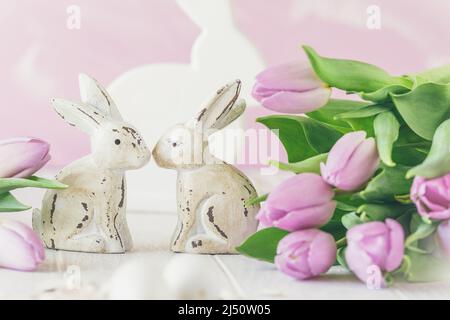 Deux lapins de Pâques en bois blanc entourés de tulipes roses fraîches, fond rose Banque D'Images