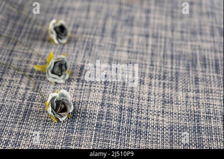 Trois fleurs grises sur fond bleu et blanc. Fleurs artificielles en tissu. Banque D'Images