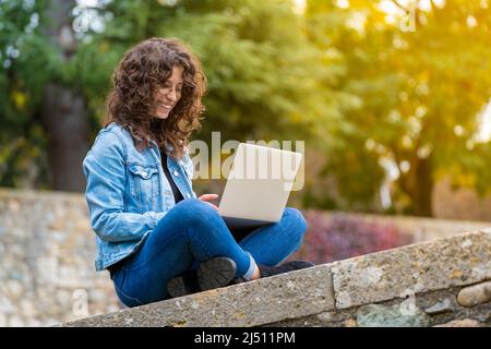 Jeune femme souriant et utilisant son ordinateur portable à l'extérieur dans le parc Banque D'Images