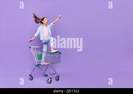 Photo de drôle impressionné petite écolière habillé jeans chemise conduite plateau shopping vide espace isolé couleur violet arrière-plan Banque D'Images