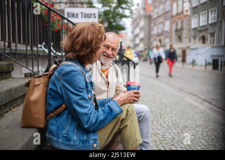 Heureux couple de touristes seniors assis sur les escaliers et ayant pris le café à l'extérieur en ville Banque D'Images