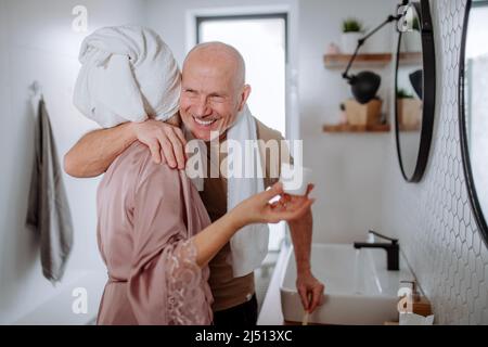 Couple senior amoureux dans la salle de bains, se brosser les dents et embrasser, concept de routine du matin. Banque D'Images