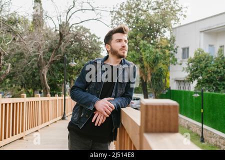 Posant, jeune homme posant avec son bras reposant sur la main courante, il a un sac sur son dos et se tient sur un pont en bois Banque D'Images