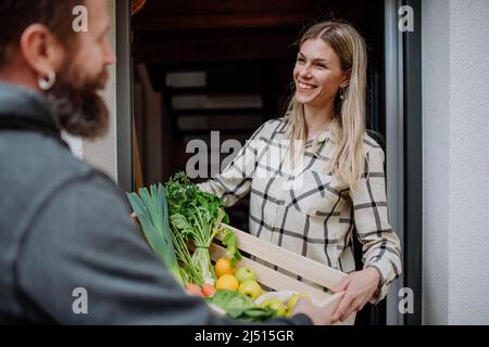 Homme mature tenant une caisse avec des légumes et des fruits et la livrant à la femme debout à la porte. Banque D'Images