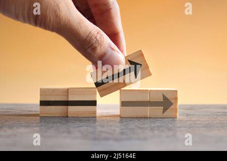 Main tenant des cubes en bois avec une icône en forme de flèche. Nouvelle stratégie, changements, alternative et amélioration Banque D'Images