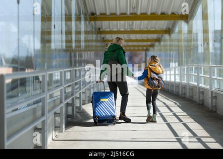 Vue arrière de mère immigrante ukrainienne avec enfant avec bagages marchant à la gare, concept de guerre ukrainienne. Banque D'Images