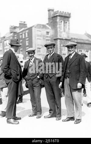 Un groupe de quatre hommes montrant les modes du 1930s, avec des chapeaux plats et des costumes. Banque D'Images