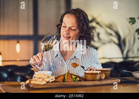 Une femme adulte heureuse dîne et prend du vin au restaurant. Banque D'Images