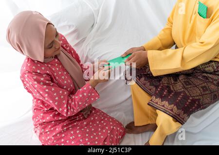 Le couple musulman célèbre la fin du Ramadan, le mois Saint islamique, donne un cadeau de paquet d'argent, cherchant le pardon, canapé blanc, fond blanc Banque D'Images