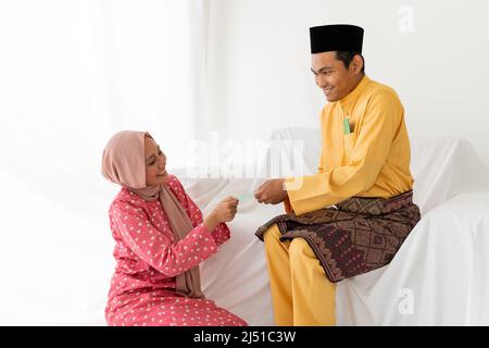 Le couple musulman célèbre la fin du Ramadan, le mois Saint islamique, donne un cadeau de paquet d'argent, cherchant le pardon, canapé blanc, fond blanc Banque D'Images