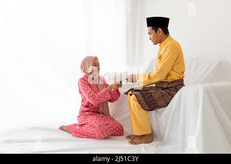 Le couple musulman célèbre la fin du Ramadan, le mois Saint islamique, donne un cadeau de paquet d'argent, cherchant le pardon, canapé blanc, fond blanc Banque D'Images