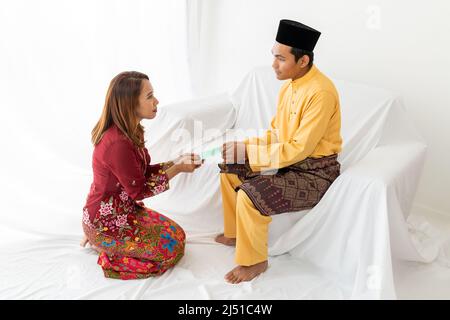 Le couple musulman célèbre la fin du Ramadan, le mois Saint islamique, donne un cadeau de paquet d'argent, cherchant le pardon, canapé blanc, fond blanc Banque D'Images