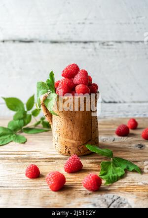Framboises dans la tasse de bois de Corkwood sur la table en bois avec des feuilles Banque D'Images