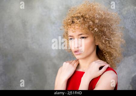 portrait latin jeune sérieux cheveux bouclés femme portant une robe rouge en plein air Banque D'Images