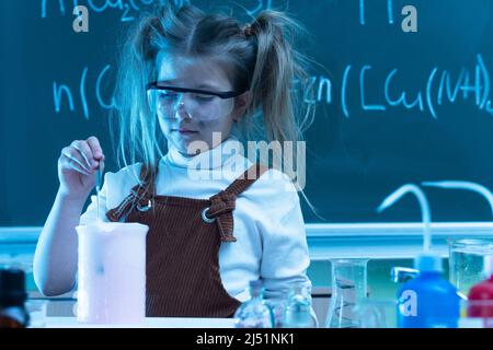 Mignonne petite fille mélange des produits chimiques pendant la leçon de chimie à l'école Banque D'Images