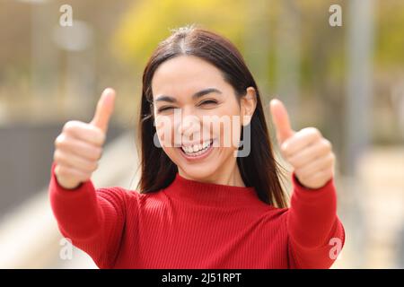 Vue de face portrait d'une femme heureuse qui fait un geste des deux pouces dans un parc Banque D'Images