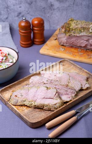 Cuisse de dinde rôtie sur un panneau en bois, coupée en morceaux. En arrière-plan se trouve un bol de salade de légumes et une dinde. Gros plan. Banque D'Images