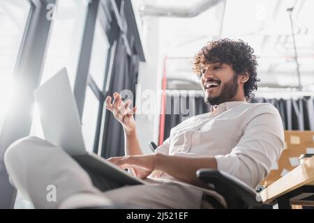 Vue en contre-plongée d'un homme d'affaires indien joyeux qui a un chat vidéo sur un ordinateur portable au bureau Banque D'Images