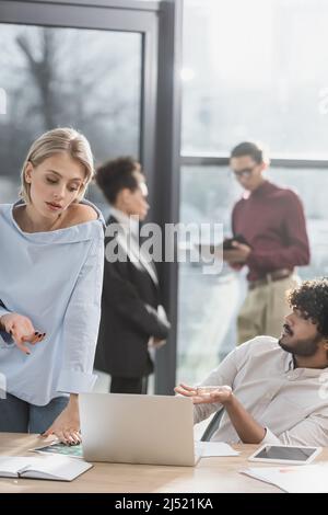 Les gens d'affaires interraciaux pointent vers un ordinateur portable près des papiers sur une table au bureau Banque D'Images