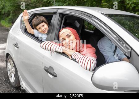 Bonne femme arabe dans hijab et enfant en branchant les mains dans la fenêtre ouverte à la voiture, mari au volant Banque D'Images