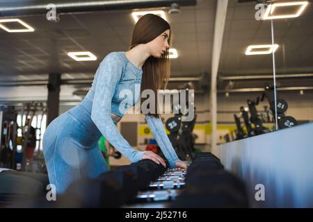 Jeune femme s'exerçant avec des haltères dans la salle de gym Banque D'Images