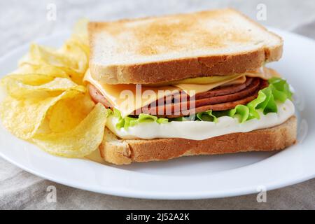 Sandwich maison au fromage et à la Bologne frits avec chips sur une assiette, vue en angle bas. Gros plan. Banque D'Images