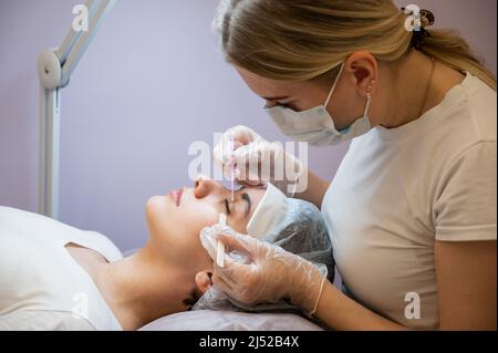 Maître peignant les cils de la femme se préparant avant la plastification. Banque D'Images