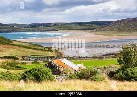 Un vieux bâtiment en pierre avec un toit en étain surplombe la grande plage de sable déserte et la mer turquoise brillante de la baie de Torrisdale, par une journée ensoleillée. Banque D'Images