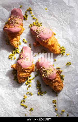 Mini-croissants au chocolat rubis et pistaches sur un papier de cuisson. Vue surharée. Banque D'Images