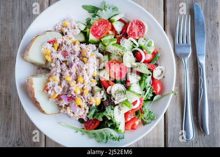 Le Tun, le maïs sucré et la mayonnaise sont servis sur une demi-pomme de terre avec une salade de légumes verts, de tomates, de concombres et d'oignons. Un aliment de base méditerranéen Banque D'Images