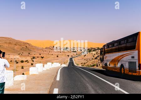 Un bus garé et un touriste méconnaissable prenant une photo avec un smartphone de la dune de sable et de la montagne reg, des clous en béton blanc le long de la route. Banque D'Images