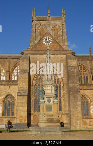 La Croix du Mémorial de Digby et une femme assise sur un banc à l'extérieur de l'abbaye de Sherborne, Sherborne, Dorset, Angleterre Banque D'Images