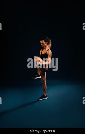 Femme de fitness qui étire sa jambe sur fond sombre. Une femme qui s'étire en studio. Banque D'Images
