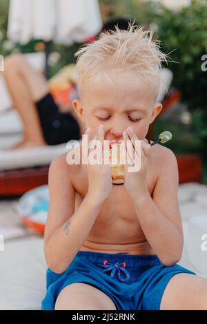 Rire mignon petit garçon ukrainien sur le camping assis et manger des fruits de pomme. Portrait d'un enfant garçon souriant heureux sur fond de nature. Petit garçon drôle Banque D'Images