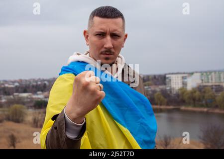 Un homme avec le drapeau de l'Ukraine montre son poing sur le fond de la ville et du lac dans la ville ukrainienne. Portrait d'un militant Ukrainien patri Banque D'Images