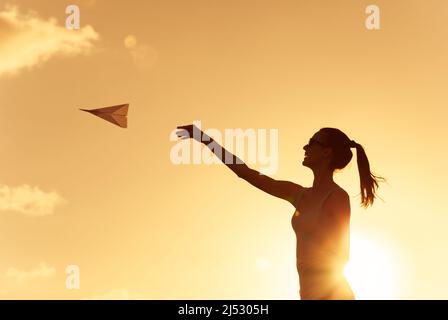 Prendre l'avion. Une femme jette un avion de papier dans le ciel. Banque D'Images