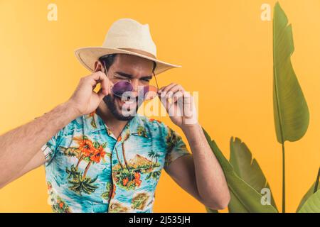 Beau Latino américain jeune homme en vêtements d'été et avec des lunettes de soleil wencant orange fond avec une plante moyenne gros plan studio tourné été concept. Photo de haute qualité Banque D'Images