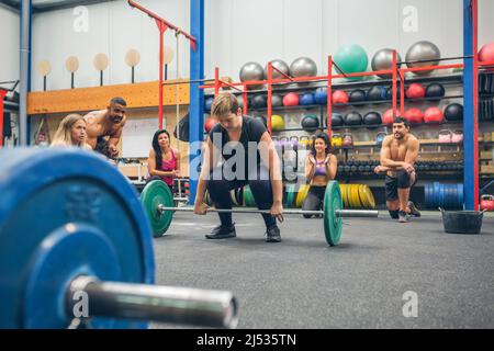 Une femme prête à faire de l'haltérophilie pendant que ses amis de gym l'applaudissent Banque D'Images